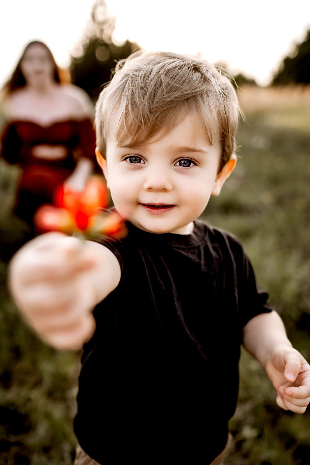A child in black clothing holding out something small while standing in a grassy field at sunset.