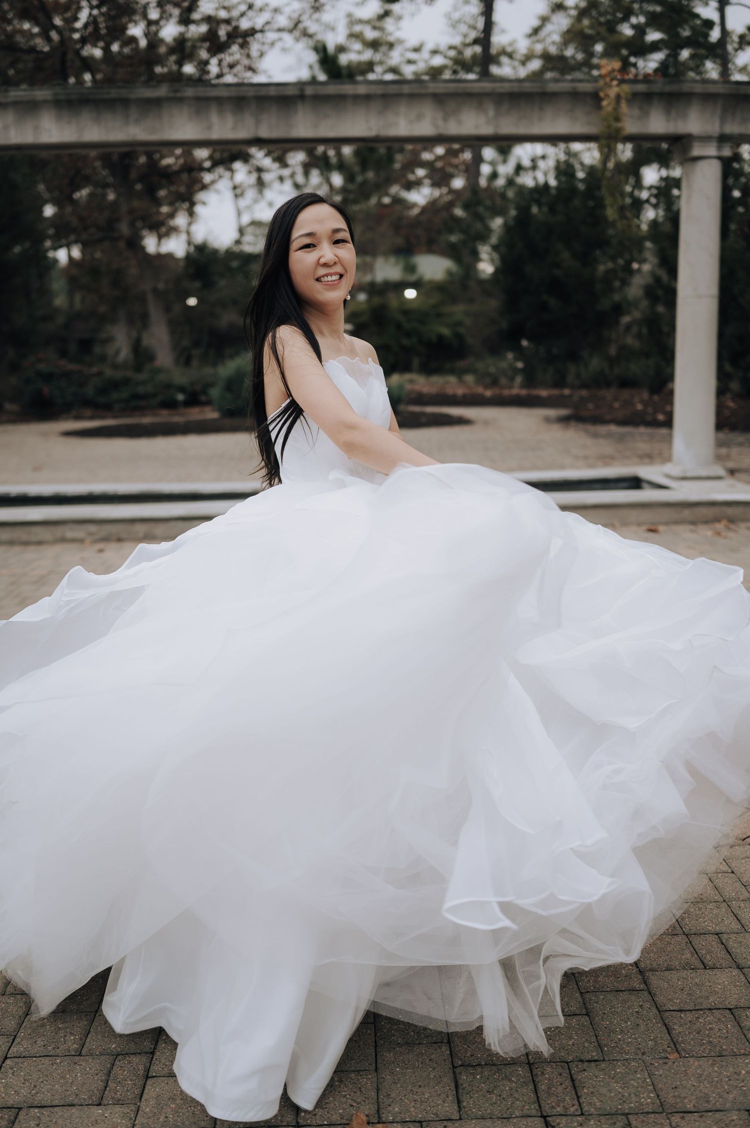 Bride in white ballgown twirls joyfully, making her dress flow in an outdoor garden setting.