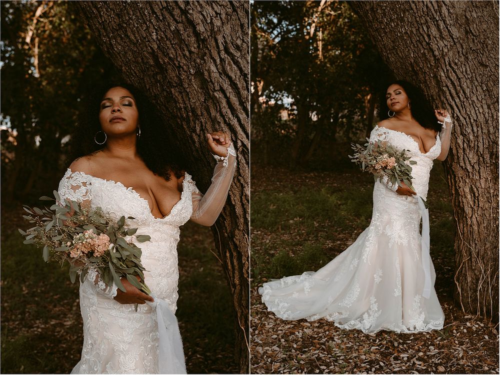 Bride in a fitted lace wedding gown poses with bouquet against large tree trunk.