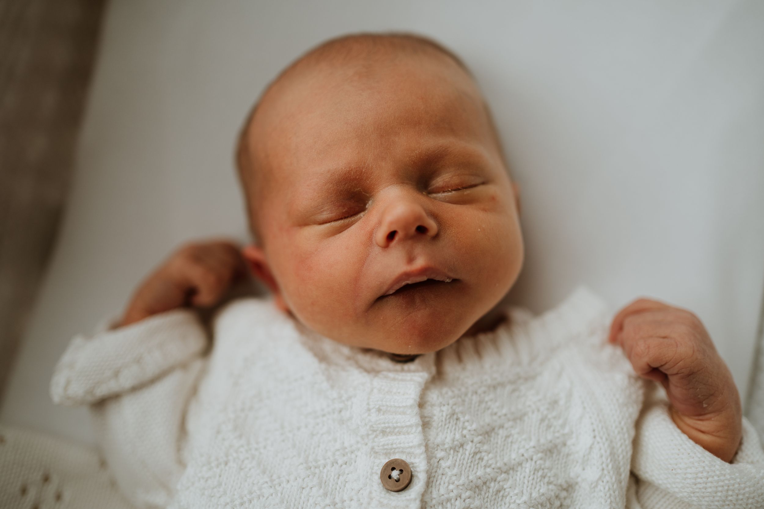 newborn baby asleep in Moses basket wearing white knitware