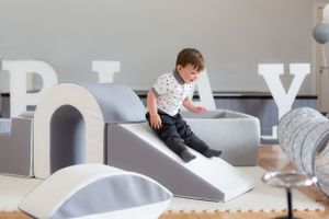 Two children sitting on gray foam furniture in playroom.