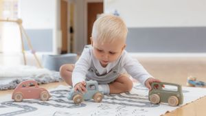 Young child plays with wooden toy cars on patterned mat in modern playroom.