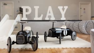 Two vintage-style pedal cars displayed in front of large PLAY text in modern playroom setting.