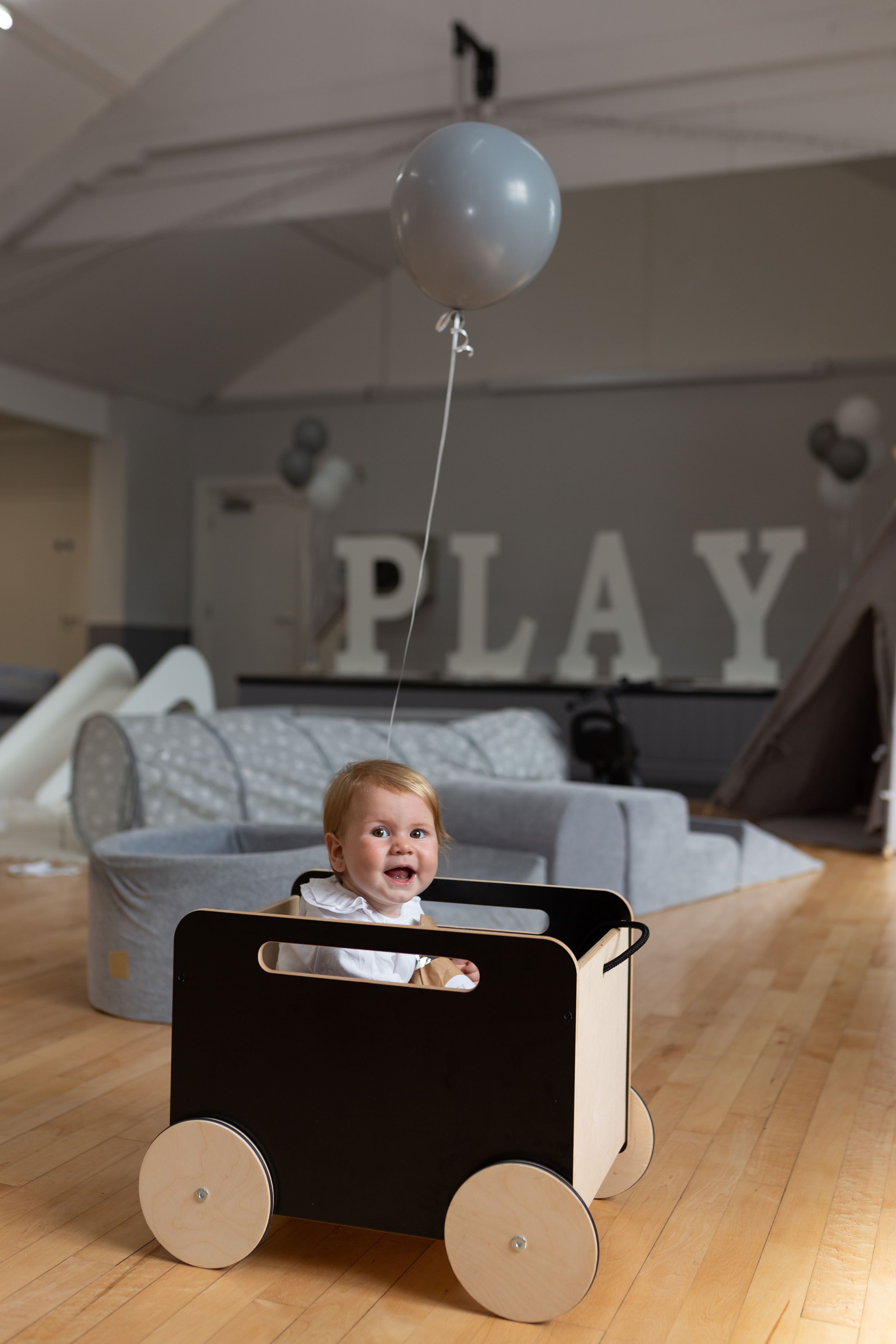 A playful moment with a toy wagon and blue balloon in a modern living room with PLAY letters on the wall.