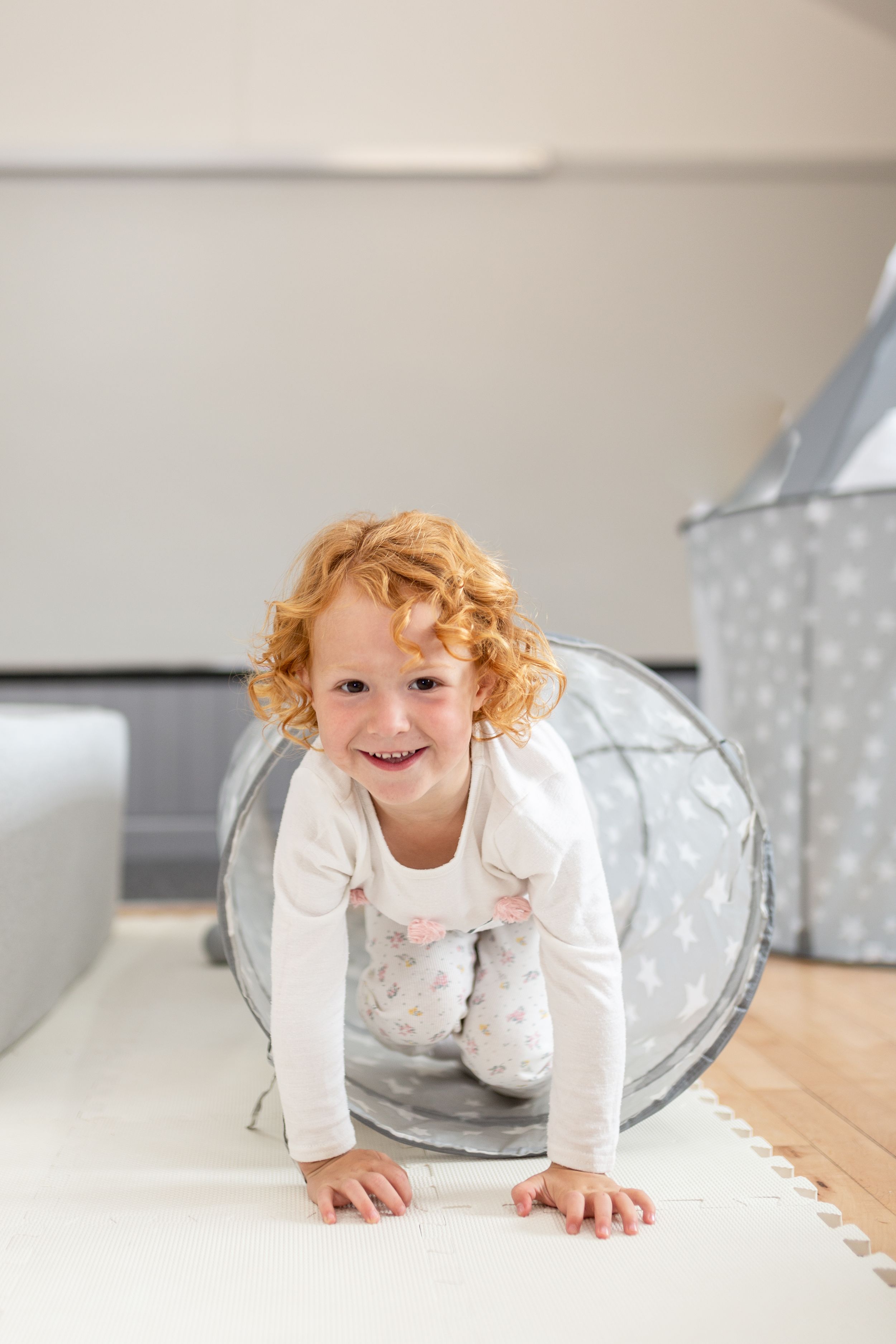 A playful moment captured crawling through a gray tunnel toy on hardwood flooring.