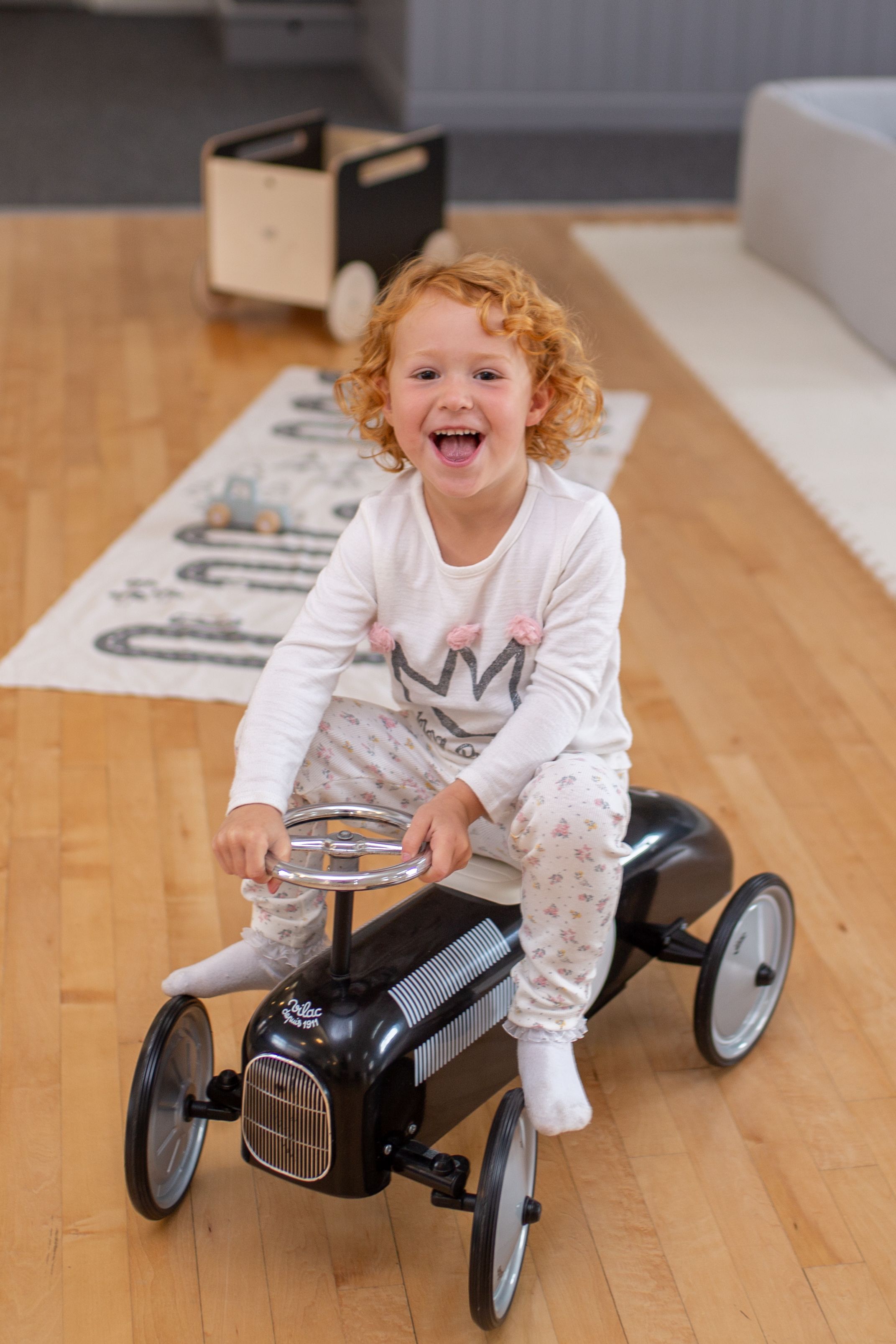 A joyful playtime scene with a vintage-style ride-on toy car on hardwood floors.