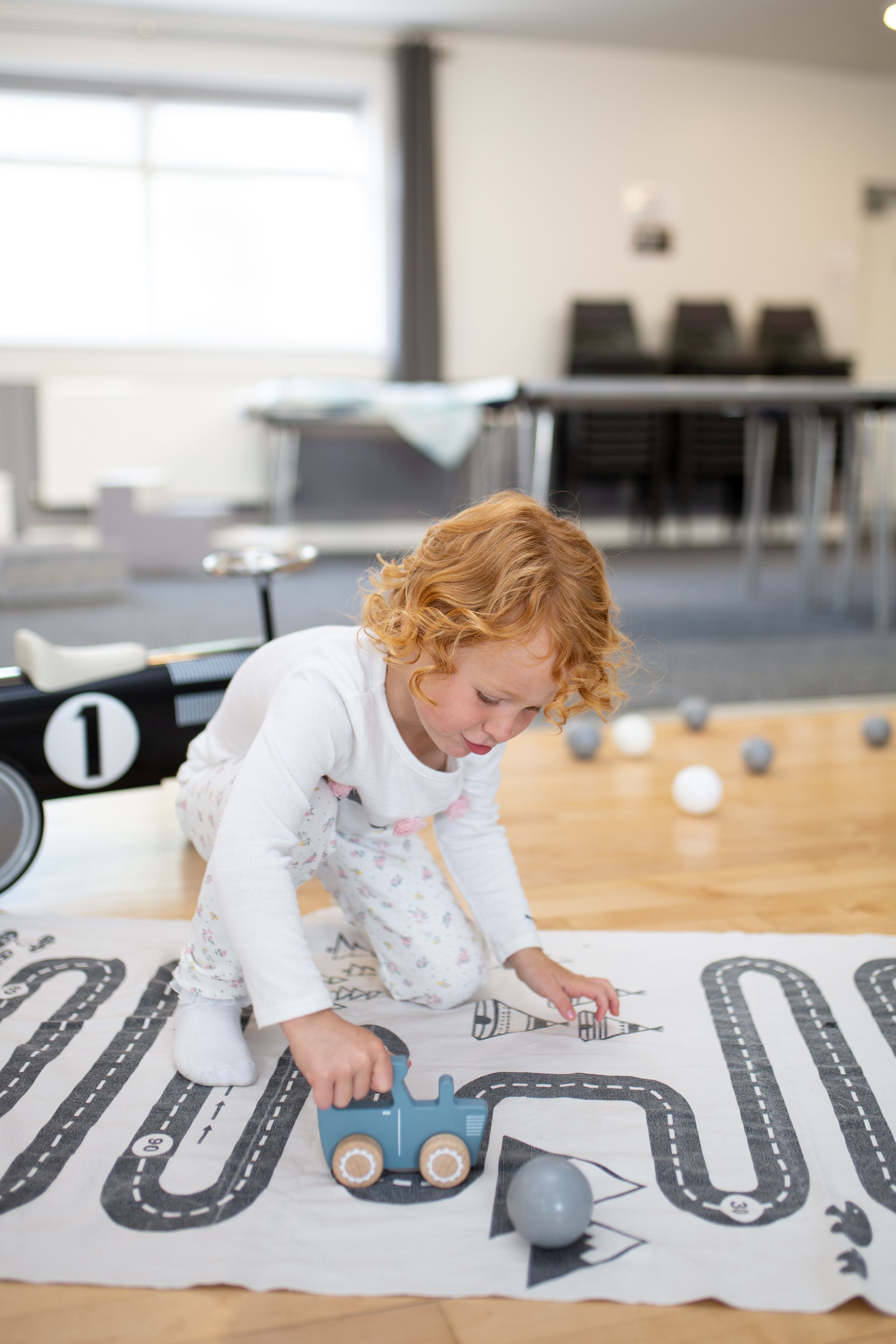 Child playing with toy car on road map playmat in classroom setting.