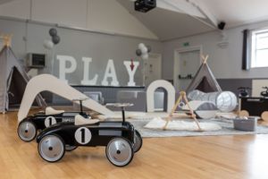 A vintage toy pedal car sits on a wooden floor with teepee tents and a 'PLAY' sign on the wall.