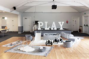 Modern playroom with white PLAY letters, slide, and vintage toys on wooden floor.