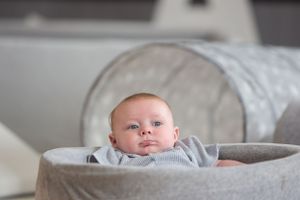 A cozy gray baby bassinet with soft padded sides in a modern nursery setting.