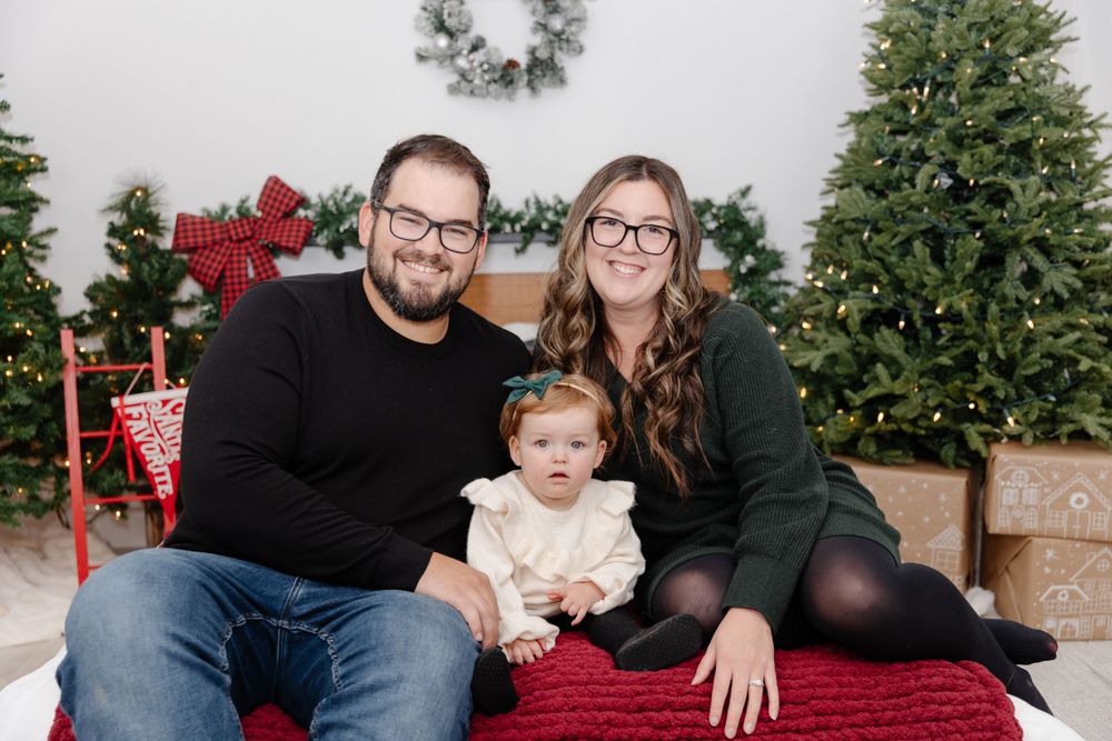 A family poses for a christmas photo in front of christmas trees.