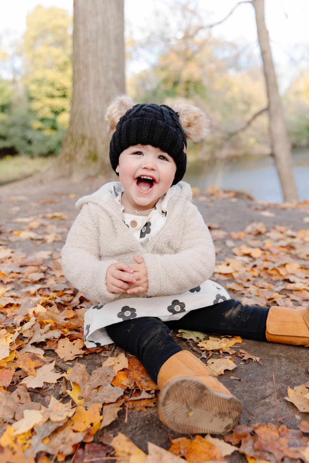 A little girl sitting in the leaves with a hat and mittens.