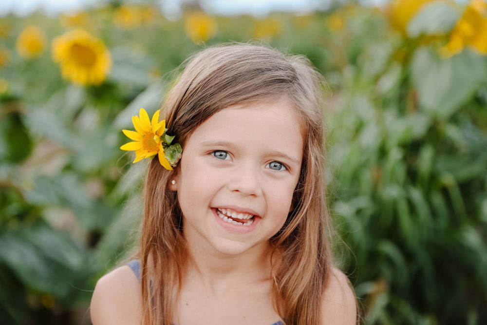 A little girl smiles in front of a field of sunflowers.