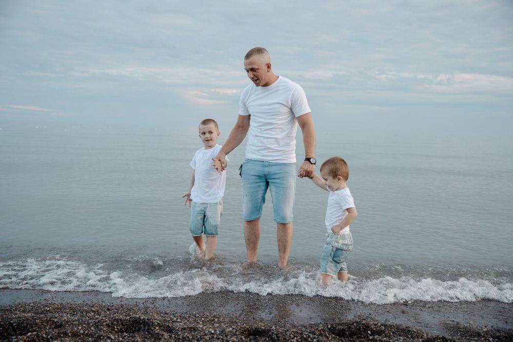 A man and his two sons are walking in the water.