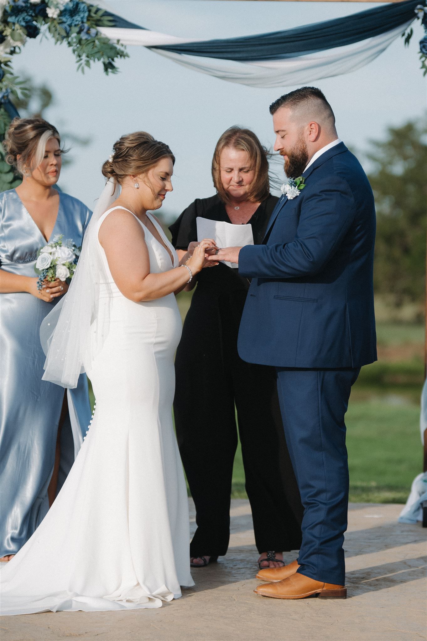 A wedding ceremony under a navy and white draped canopy with a couple exchanging vows.