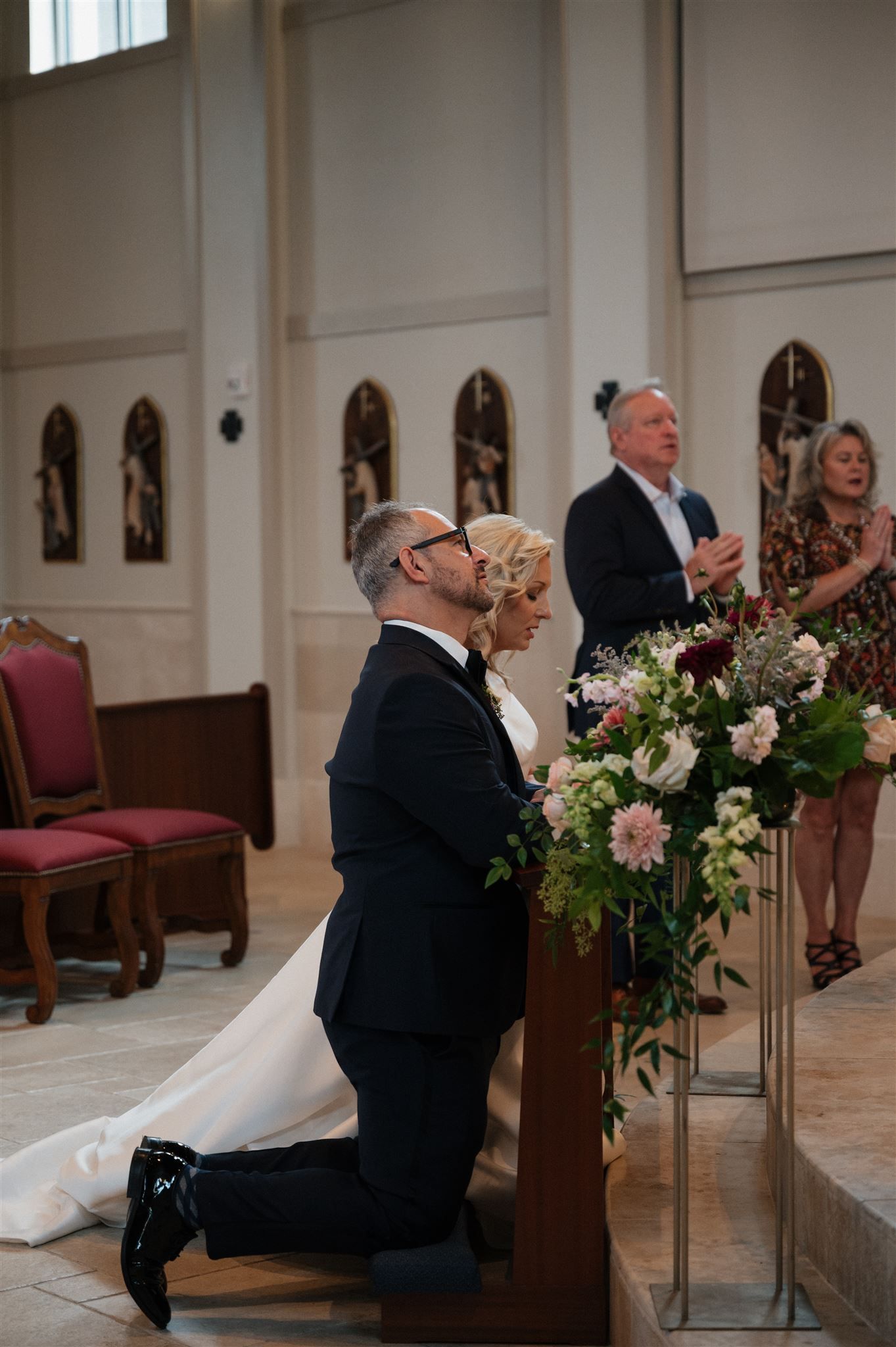 A person kneels in prayer at the altar during a wedding ceremony surrounded by floral arrangements.