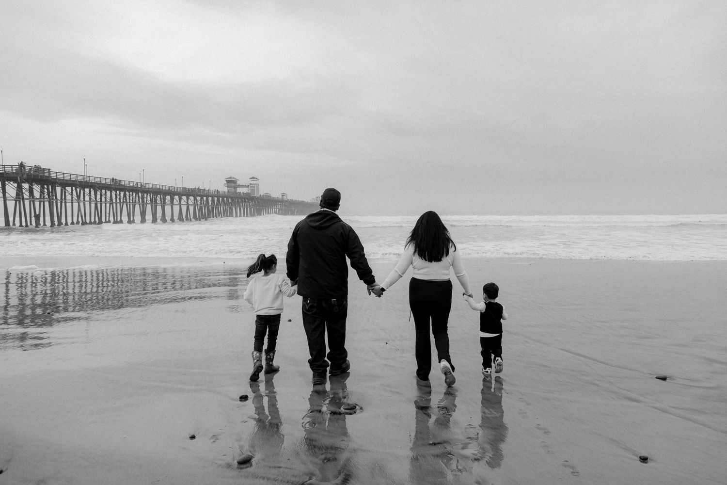 Silhouette of family walking along a misty beach with a pier in the background.