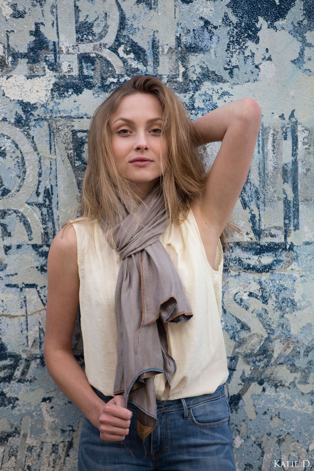 Woman wearing a simple taupe lightweight scarf tied loosely around neck with cream top.