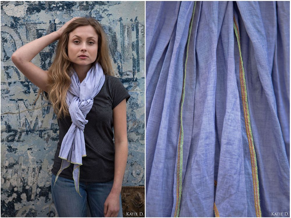 Woman in black top wearing a light purple blue linen scarf with gold trim.