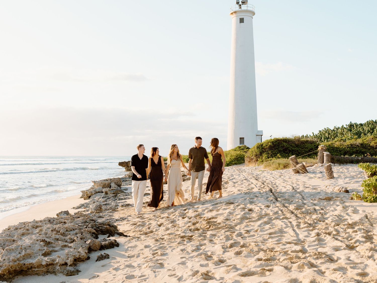 A family photoshoot by Moments With Kell on Oahu in Hawaii with a family of five holding hands on the beach