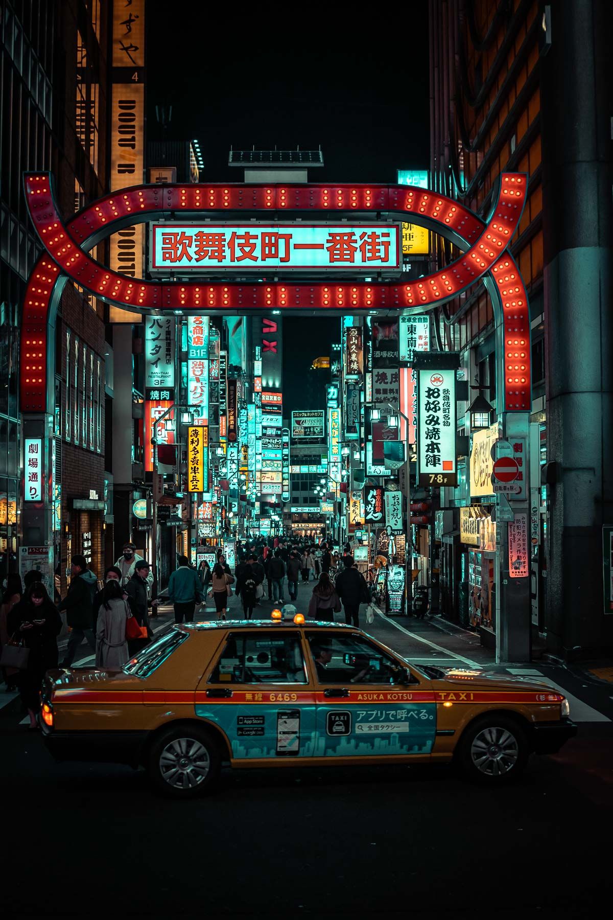 Vibrant red gateway arch with Japanese text over a busy street with taxis and neon signs in Tokyo.