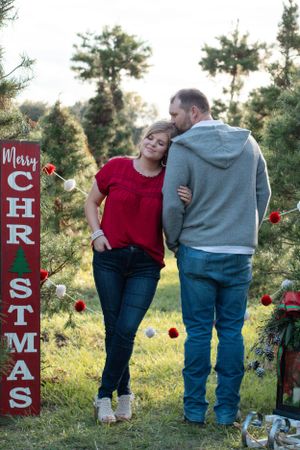 Couple sharing intimate moment by Christmas sign and decorated evergreens at sunset.