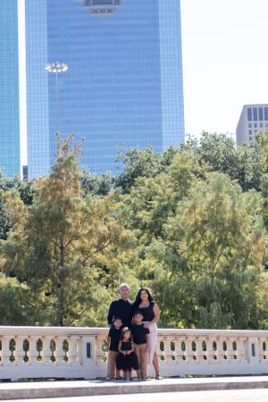 Family poses on marble balcony with modern blue skyscraper and trees in background.