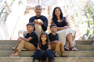A family of five sits together on outdoor stone steps on a sunny day.