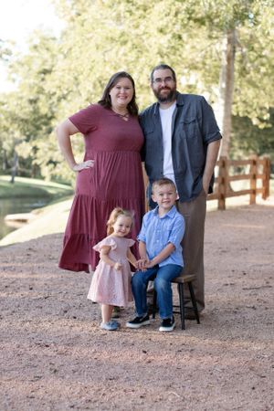 Family portrait with two small children standing together on a dirt path near wooden fencing.
