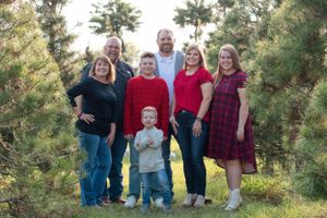 Family group portrait with Christmas trees and decorative ornaments in outdoor setting.