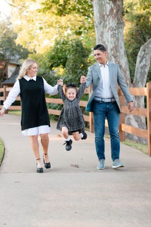 Family walking on a path lifting a child playfully between them on a sunny day.