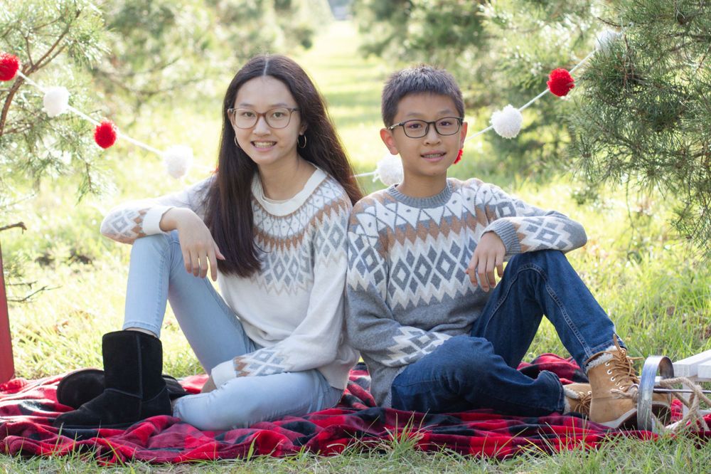 Couple in matching fair isle sweaters sits on red blanket for holiday photos.