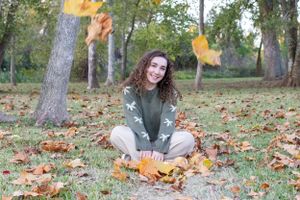 A relaxed autumn portrait sitting among fallen leaves in casual attire.