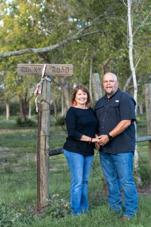 Couple standing by rustic wooden road sign post in rural outdoor setting.