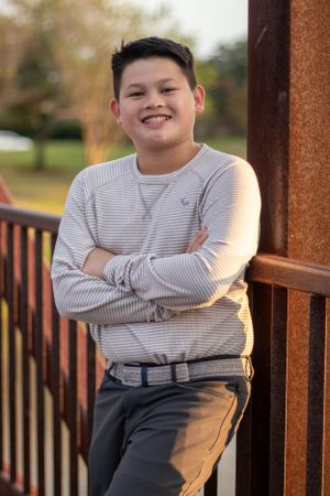 Young student in a striped sweater poses confidently with crossed arms on an outdoor deck.