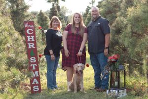 A holiday family portrait with a golden retriever and Christmas decorations at a tree farm.