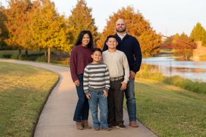 Family of four poses together on a walking path during autumn with colorful fall foliage in the background.