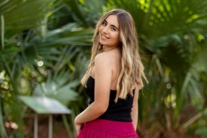 A woman in a black top poses in a tropical garden setting.