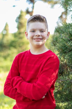 Portrait of someone in bright red sweater standing next to evergreen tree.