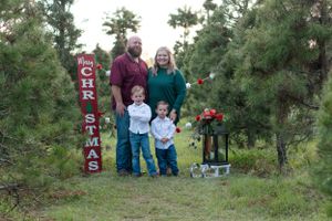 A festive family photo at a Christmas tree farm with a red and white decorative sign and lantern display.