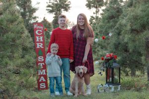 A holiday portrait at a Christmas tree farm with decorative sign and golden retriever.