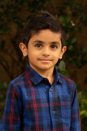 A young boy wearing a blue and red plaid button-down shirt smiles at the camera.