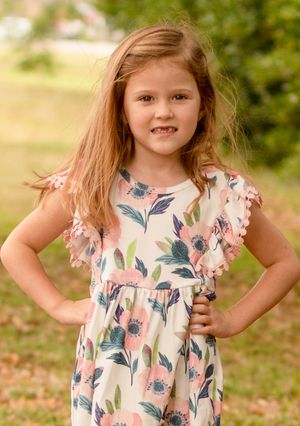 A young girl in a floral dress with ruffled sleeves poses outdoors in natural lighting.