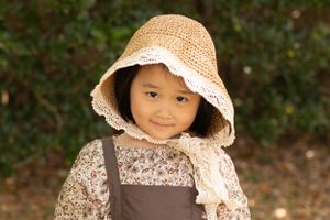 A child wearing a vintage-style bonnet and floral dress poses for a portrait.