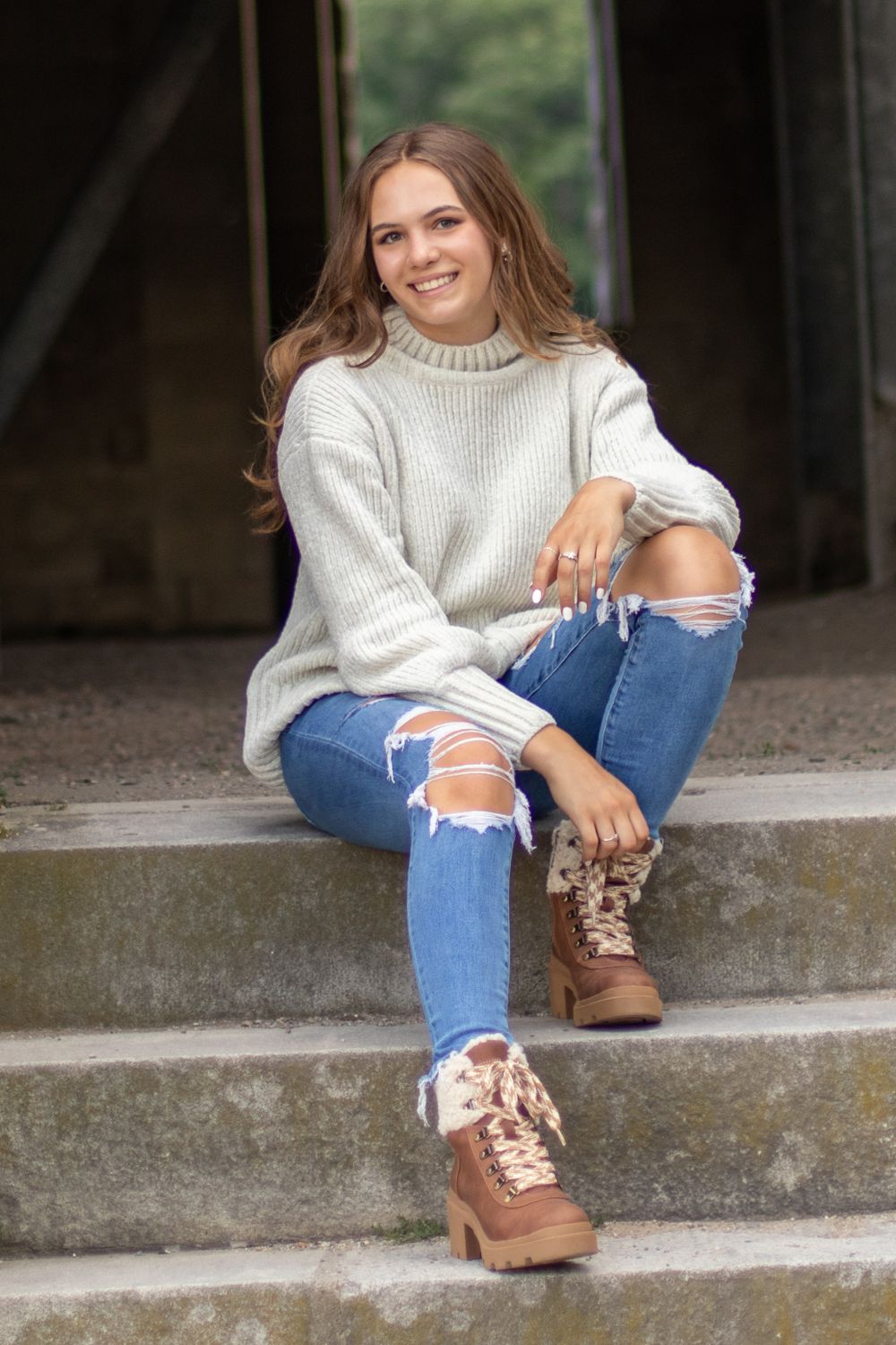 A person in a cozy sweater and distressed jeans sits on concrete steps.