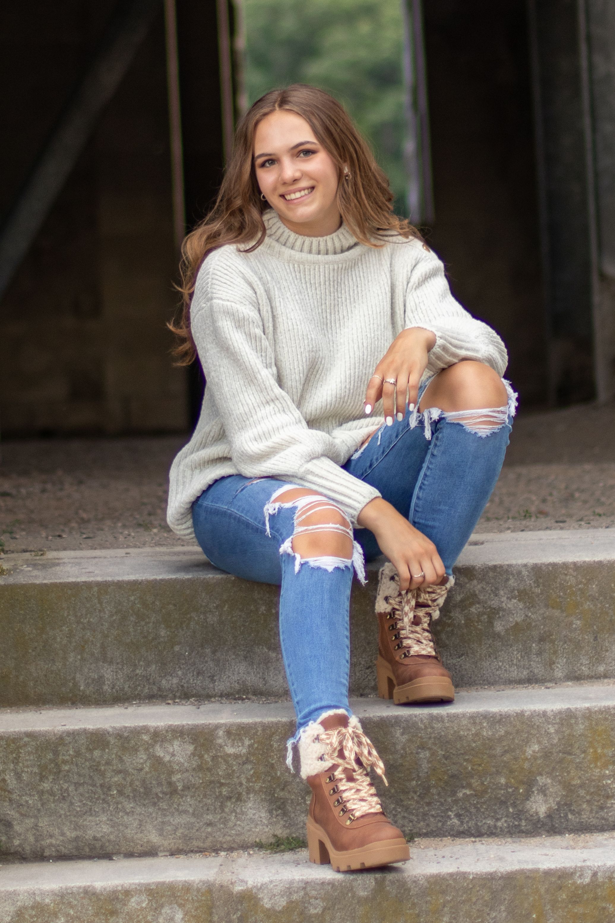 A person in a cozy sweater and distressed jeans sits on concrete steps.