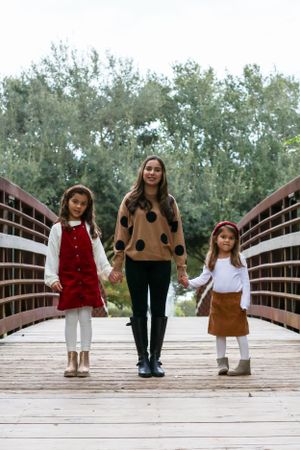 Three people pose on wooden bridge wearing fall fashion outfits.
