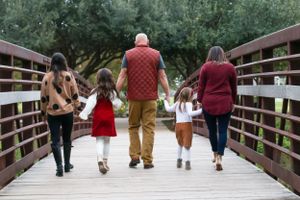 Family of five walking together on wooden bridge through park.