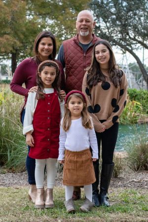 Family of five poses together outdoors in coordinated fall outfits.