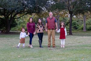 Family group walks together on grass with trees in background.